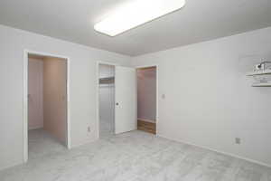 Unfurnished bedroom featuring a spacious closet, light colored carpet, and a textured ceiling