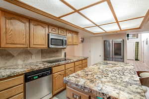 Kitchen featuring stainless steel appliances, a kitchen island, light stone countertops, tasteful backsplash, and a kitchen bar
