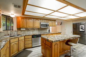 Kitchen featuring stainless steel appliances, backsplash, a center island, light stone countertops, and a breakfast bar area