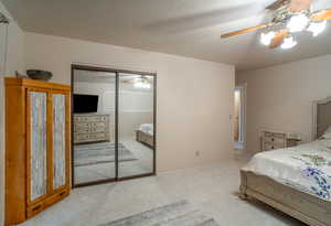 Bedroom with light colored carpet, ceiling fan, a textured ceiling, and a closet