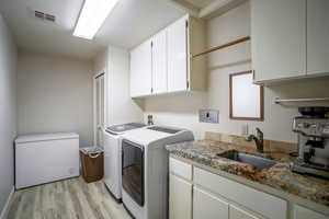 Laundry room with light wood-style flooring, separate washer and dryer, and cabinet space