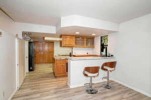 Kitchen with brown cabinets, glass insert cabinets, a peninsula, a kitchen bar, and light wood-style flooring