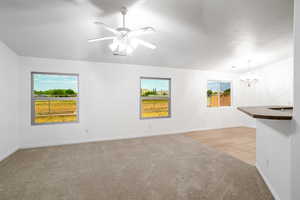 Unfurnished room with light colored carpet, a chandelier, and a ceiling fan