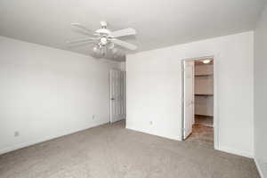 Unfurnished bedroom with light colored carpet, a walk in closet, and ceiling fan
