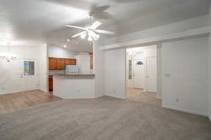 Unfurnished living room featuring a chandelier, vaulted ceiling, light carpet, and ceiling fan