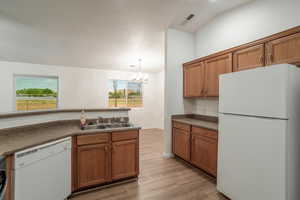 Kitchen featuring white appliances, brown cabinets, dark countertops, and light wood-style floors