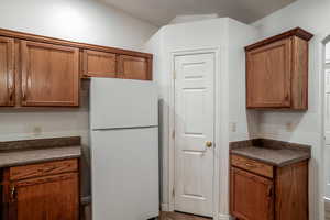 Kitchen with freestanding refrigerator, dark countertops, and brown cabinetry