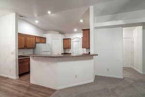 Kitchen with brown cabinetry, freestanding refrigerator, a peninsula, recessed lighting, and lofted ceiling