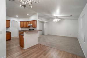 Kitchen with brown cabinetry, light wood finished floors, arched walkways, vaulted ceiling, and open floor plan