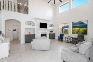 Living room featuring arched walkways, a high ceiling, a fireplace, light tile patterned flooring, and a ceiling fan