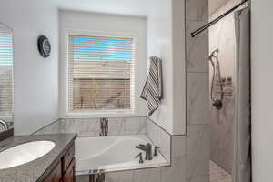 Bathroom featuring a garden tub, a marble finish shower, and vanity