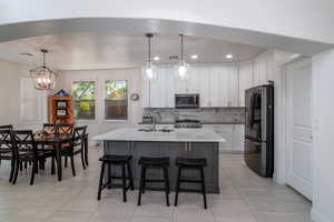 Kitchen with appliances with stainless steel finishes, white cabinetry, decorative backsplash, light tile patterned floors, and a center island with sink
