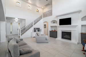 Living room featuring built in features, a glass covered fireplace, stairs, a high ceiling, and light tile patterned floors