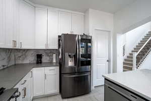 Kitchen with stainless steel appliances, light tile patterned floors, backsplash, and white cabinetry