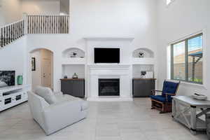 Living area with a towering ceiling, a glass covered fireplace, arched walkways, light tile patterned floors, and built in features