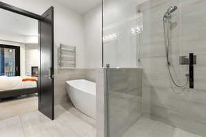 Bathroom featuring a freestanding bath, a towel warming rack, tile walls, and a shower stall