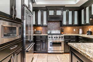 Kitchen featuring glass insert cabinets, decorative backsplash, dark cabinetry, and high quality appliances