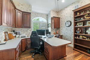 Home office with wallpapered walls, dark wood-style floors, and built in desk