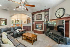 Living area featuring a chandelier, a glass covered fireplace, light colored carpet, built in shelves, and ceiling fan