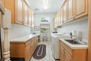Laundry area with light tile patterned flooring, washing machine and clothes dryer, and cabinet space
