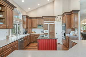 Kitchen with plenty of natural light, high vaulted ceiling, built in appliances, tasteful backsplash, and dark wood finished floors
