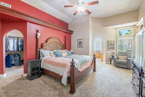 Bedroom with arched walkways, light carpet, ceiling fan, a walk in closet, and high vaulted ceiling