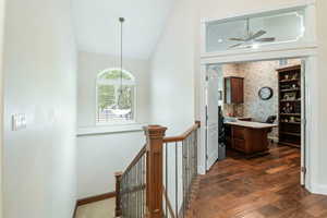 Corridor featuring an upstairs landing, dark wood-style floors, vaulted ceiling, and wallpapered walls
