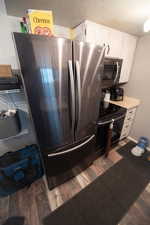 Kitchen view of appliances with stainless steel finishes, a textured ceiling, dark wood-style floors, light countertops, and white cabinetry