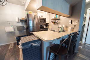 Kitchen with a kitchen bar, appliances with stainless steel finishes, white cabinets, dark wood-style floors, and light countertops