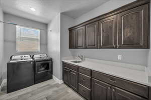 Laundry area featuring a textured ceiling, light wood finished floors, separate washer and dryer, and cabinet space