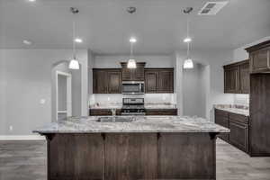 Kitchen featuring arched walkways, a kitchen breakfast bar, dark brown cabinetry, appliances with stainless steel finishes, and recessed lighting