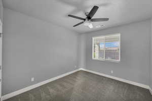 Spare room featuring dark colored carpet and a ceiling fan