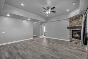 Unfurnished living room with arched walkways, a stone fireplace, a raised ceiling, light wood-style floors, and ceiling fan