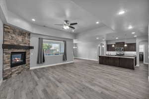 Unfurnished living room with arched walkways, a ceiling fan, a fireplace, a raised ceiling, and light wood-type flooring