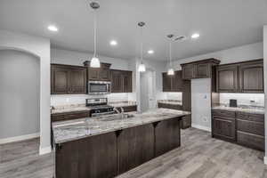 Kitchen with arched walkways, dark brown cabinets, light stone countertops, hanging light fixtures, and recessed lighting