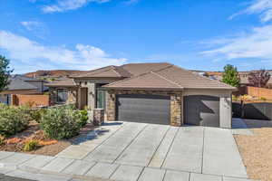 View of front facade featuring an attached garage, a tile roof, concrete driveway, stucco siding, and stone siding