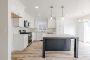 Two tone kitchen featuring stainless steel appliances, light wood-type flooring, a breakfast bar area, a kitchen island, and dual tone cabinets