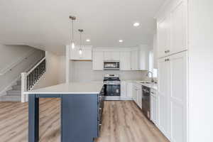 Kitchen with two tone color scheme, stainless steel appliances, light wood-type flooring, decorative light fixtures, and a kitchen bar