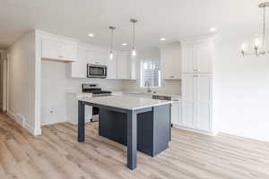 Kitchen with stainless steel appliances, two tone color scheme, a kitchen island, light wood-style floors, and a breakfast bar