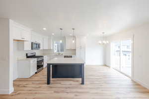 Kitchen featuring stainless steel appliances, a kitchen island, light wood-style floors, suspended lighting, and a kitchen breakfast bar