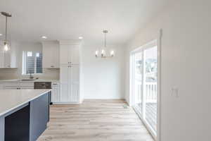 Dual tone kitchen featuring two tone cabinets, a chandelier, light wood-type flooring, light stone countertops, and stainless steel dishwasher