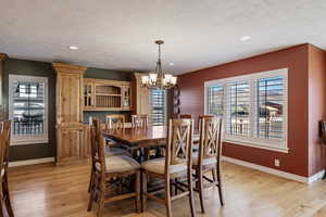 Dining space with healthy amount of natural light, light wood finished floors, a chandelier, a textured ceiling, and recessed lighting