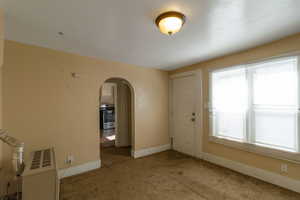 Empty room with arched walkways, carpet floors, and heating unit