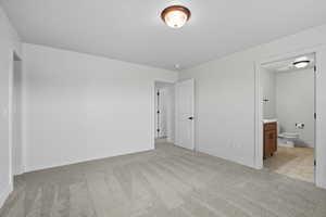 Unfurnished bedroom featuring light carpet and ensuite bathroom