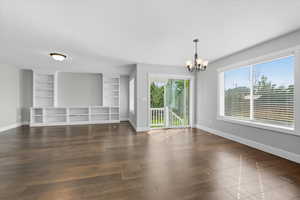 Unfurnished living room with dark wood-style flooring, a chandelier, and built in features