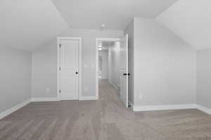 Bonus room with vaulted ceiling and light colored carpet