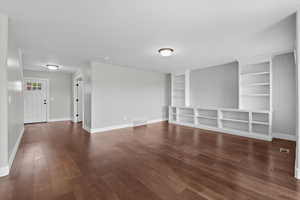 Unfurnished living room featuring dark wood-style flooring and built in shelves