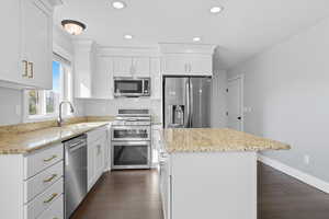 Kitchen featuring white cabinets, stainless steel appliances, a kitchen island, recessed lighting, and dark wood-type flooring