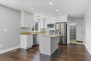 Kitchen with stainless steel appliances, light stone countertops, a kitchen island, white cabinets, and recessed lighting