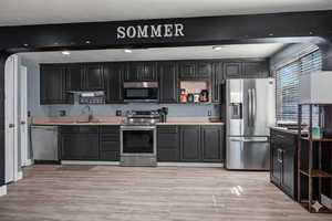 Kitchen with open shelves, appliances with stainless steel finishes, light countertops, light wood-style floors, and recessed lighting